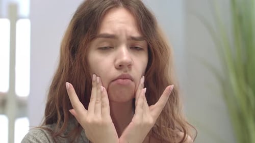 Adolescente molesta mirando la piel problemática y tocándose la cara en el baño delantero