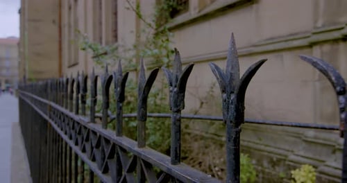 Black wrought iron fence against a sandstone cathedral wall. Static shot.