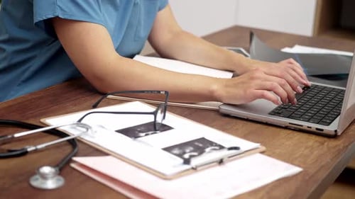 Medical Professional Typing and Taking Notes at Desk