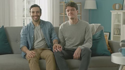 Affectionate young men hold hands on a sofa
