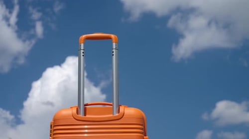 Orange Suitcase with Handle Against Blue Sky with Clouds