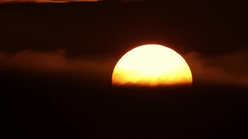 A Huge Yellow Round Sun Sets Behind Black Tense Clouds