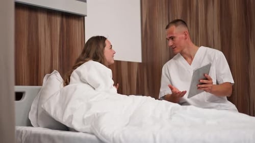 in Modern Clinic in a Bright VIP Room a Young Girl in a White Coat Lies on the Bed Consulting a