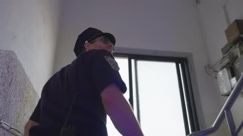 Police officer climbing up stairs inside city building during daytime. Back view following cop looki