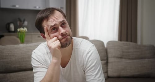 Man Sitting at Home on the Couch Ponders Focused Action Plan Holds Hand Near Face Sitting at Home on