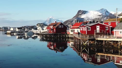 Red cabin by the water with mountains in the background during golden hour in Norway