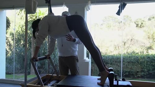 Woman Doing Pilates on Reformer Machine with Instructor