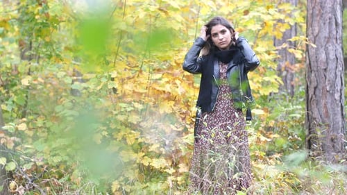 Wide shot of Brunette girl in autumn forest, stands thoughtfully and looks into the camera while she