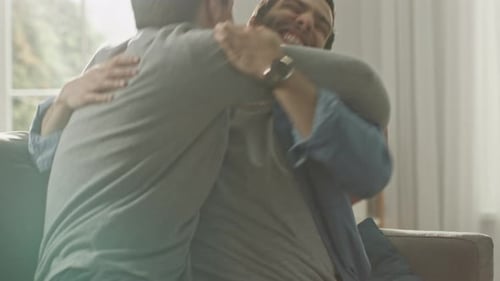 Two Men Hugging on Couch in Bright Home