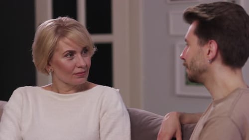 Hijo adulto sonriente hablando con su madre en el sofá El hijo adulto conversa con su madre