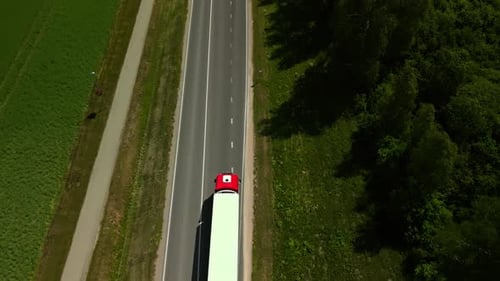 The Red Truck Drives Along a Rural Road in Serene Countryside with Lush Greenery Under a Peaceful