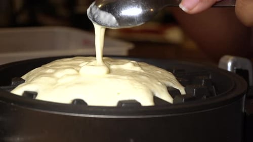 Spreading waffle batter on a waffle iron for a homemade breakfast - isolated close up