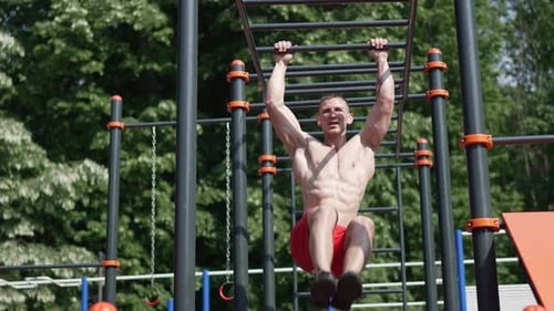Athletic Man Hanging on Monkey Bar While Exercising on Sports Ground