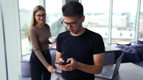 Colleagues at office during the lunch break. Man holding a phone and woman comes up to help him.