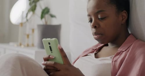 Happy Young Lady Browsing with Smartphone Relaxing at Home Sitting in Bed Using Device