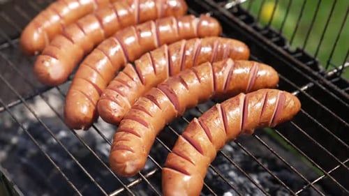 Sausages on a barbeque grill. Juicy sausages cooking over hot charcoal in smoke.