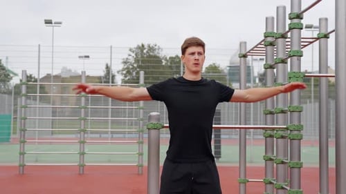 Young Sporty Man Warming Up Shoulders and Arms in Outdoor Park