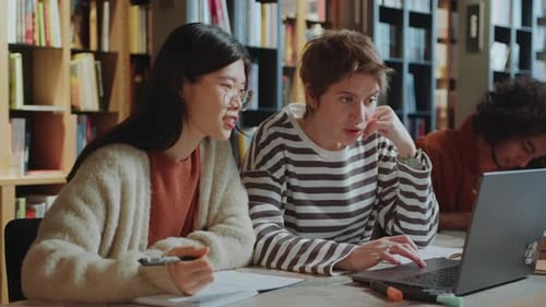 Two Diverse College Girls Discussing Project on Laptop in Library