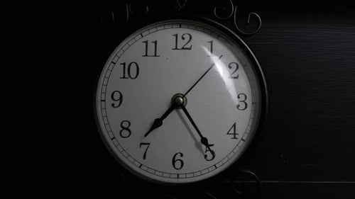 Zeitraffer einer kleinen schwarzen Uhr in einem schwach beleuchteten Raum.