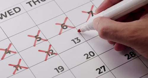 Hand Crossing Off Days On Calendar With Red Marker