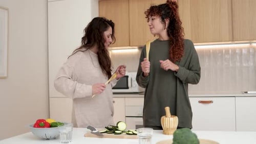 Felices amigas latinas divirtiéndose bailando con música mientras cocinan juntas en la cocina de casa
