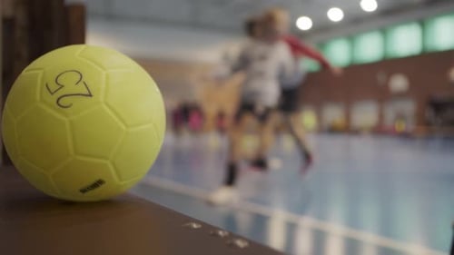 Static shot of a yellow handball. In the background, teams are practicing before a handball match.
