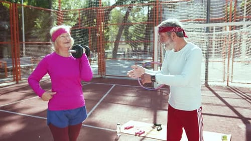Senior Couple Exercising With Dumbbell in Urban Court
