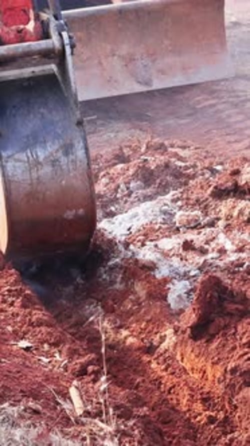 Excavator Digging Deep Trench in Red Soil