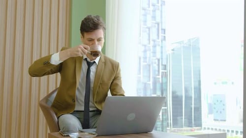 Young Adult Works on Laptop, Sips Coffee