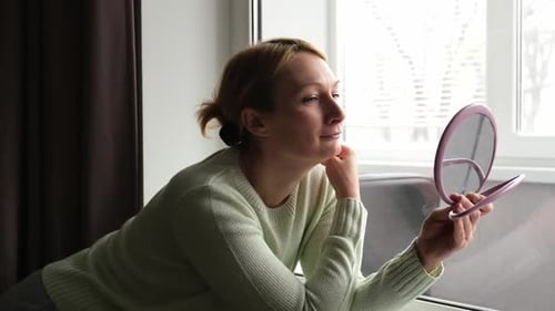 Woman Checks Her Face with a Handheld Mirror