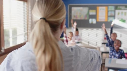 In school, female teacher calling on students raising hands in classroom discussion