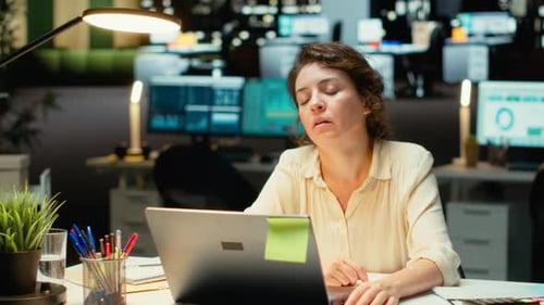 Woman working on laptop in busy office at night