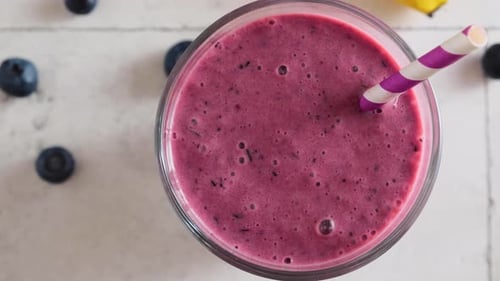 Top View of Glass of Blueberry and Banana Smoothie with a Straw on the Table Healthy Summer