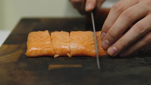 Slow motion close up of male chef cutting fresh salmon fillet in several pieces