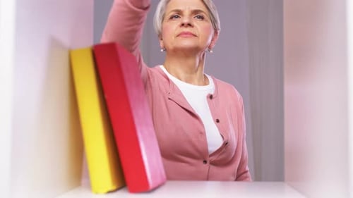 Senior Woman Dusters Books on Shelf Inside Home
