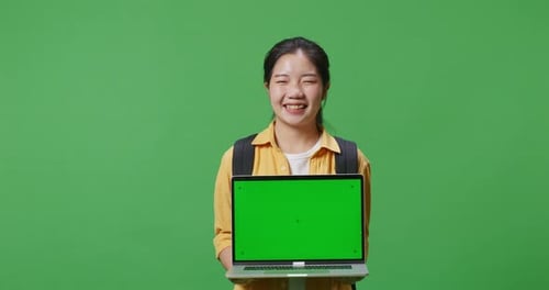 Asian Woman Student With A Backpack Smiling And Showing Green Screen Laptop In The Green Screen