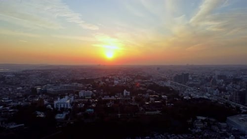 A city skyline at sunset with radiant sun casting hues of orange and blue, aerial view