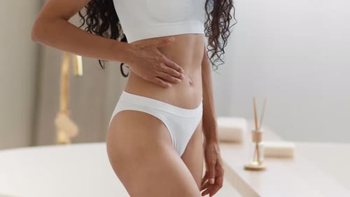 Lose Up Shot einer nicht wiedererkennbaren jungen Frau in Unterwäsche, die langsam Hautstraffungscreme auf ihren Bauch reibt