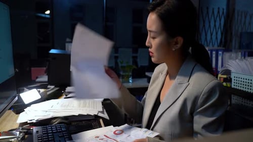 Young businesswoman feeling overwhelmed by mountain of paperwork. She is feeling stressed frustrated