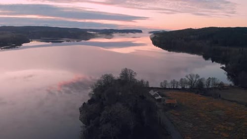 Aerial view of a pink sunset sky reflecting into a calm lake, wide shot, drone flying forward