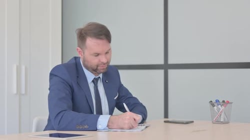 Businessman Writing in Notebook in Office
