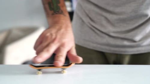 Man Plays Fingerboard On Table And Performs Cool Skateboarding Gestures