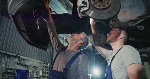 At the Auto Service Handsome Young Auto Mechanics in Uniform are Smiling While Repairing Car
