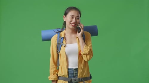 Asian Female Hiker Smiling And Talking On Smartphone While Standing On Green Screen