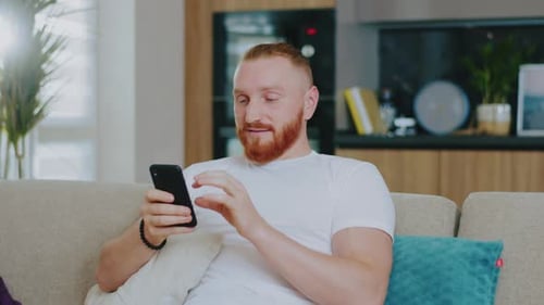Man using mobile phone at home on sofa