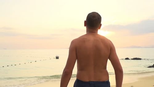 Young man walks carefree on tropical beach at sunset super slow motion