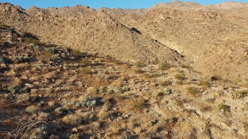 Drone shot rising slowly then moves forward quickly over ridge of arid mountain.