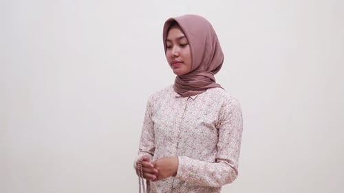 Young asian muslim woman standing while praying using prayer beads