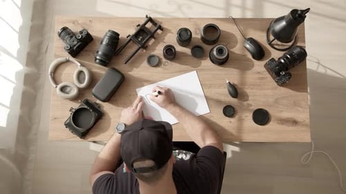 Freiberuflicher Videofilmer am Schreibtisch schreibt Inschrift auf Papier Teil Eins