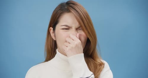 Asian lady wear sweater over blue isolated background smell something stinky and disgust.